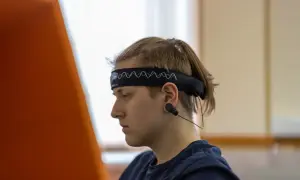 Młody mężczyzna w opasce z elektrodami do eeg w czuwaniu, skupiony na czymś poza kadrem.