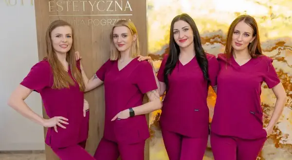 Cztery kobiety w uniformach medycznych stoją obok siebie przed tablicą z napisem "Kosmetologia Estetyczna".