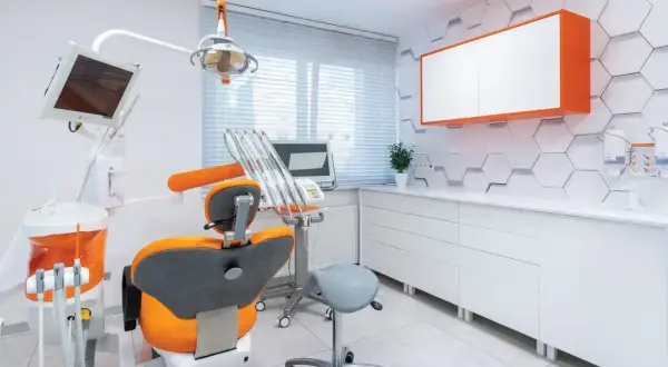 Nowoczesny gabinet stomatologiczny z fotelem dentystycznym w kolorze pomarańczowym i białymi meblami.