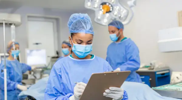 Zespół medyczny przygotowuje się do operacji. Pielęgniarka notuje informacje, być może dotyczące tego, ile trwa operacja usunięcia nerwiaka.