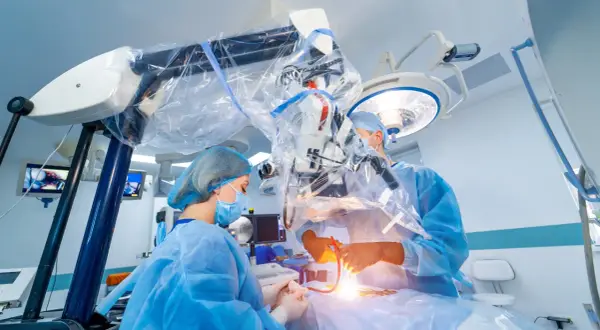 Chirurdzy w sterylnych strojach prowadzą skomplikowaną operację neurochirurgiczną pod mikroskopem.