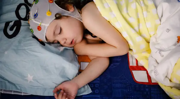 Dziecko śpi w czepku z elektrodami do badania EEG. Czas badania zależy od celu, ale często trwa kilka godzin.