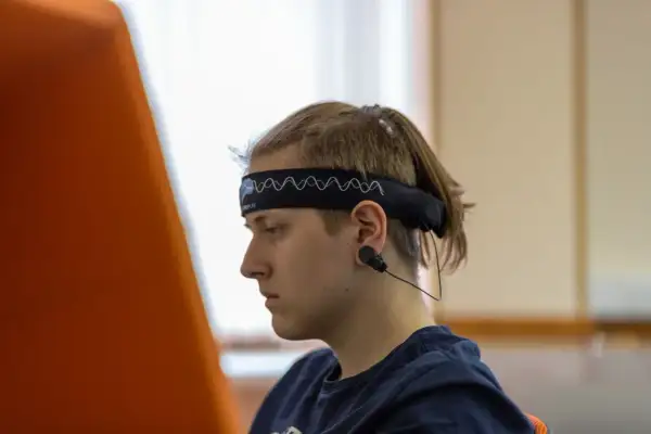 Młody mężczyzna w opasce z elektrodami do eeg w czuwaniu, skupiony na czymś poza kadrem.